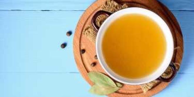A top view of a pot of Homemade Chicken Broth on a blue background.