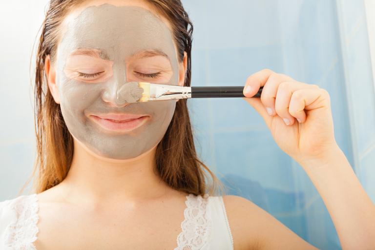 a teenage girl applying a gray mud facial mask