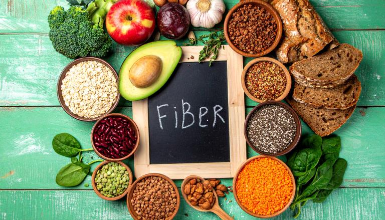 The word fiber on a blackboard slate surrounded by food sources of fiber, like avocado, beans, and lentils.
