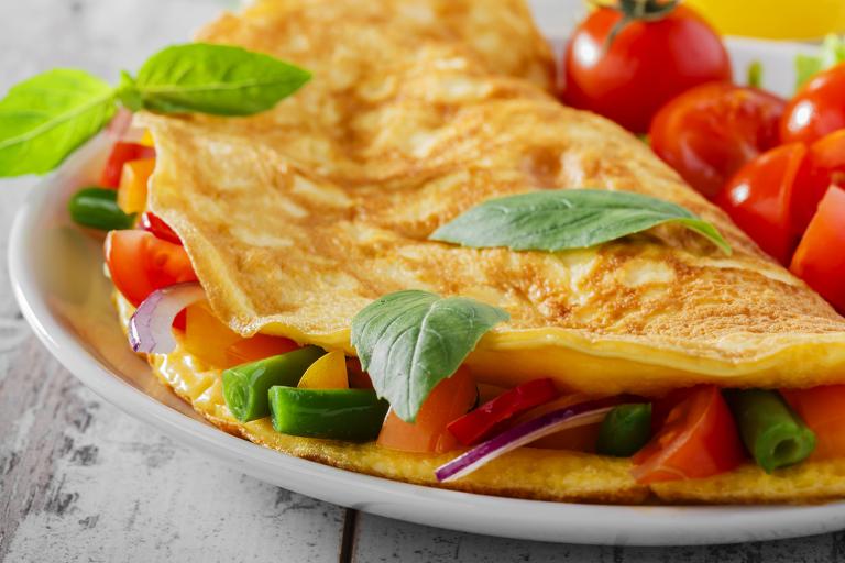 a perfectly-cooked omelet with veggies and chopped cherry tomatoes